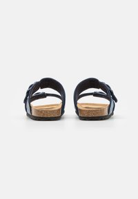 Sanda negra con dos correas ajustables, plantilla de corcho y suela de goma texturizada. La vista trasera muestra el talón abierto y un diseño minimalista.