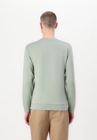 Sweatshirt de manga comprida verde menta com decote redondo e punhos canelados, combinado com calças castanhas claras. Textura suave.