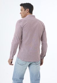Camisa de manga larga a rayas rojas y blancas con cuello abotonado, que presenta un diseño ajustado y un dobladillo redondeado, combinada con jeans de color azul claro.