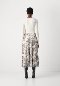 Witte lange mouwtop gecombineerd met een geplooide midi-rok met een zwart-wit abstract kaartmotief. Zwarte haklaarzen maken de outfit af.