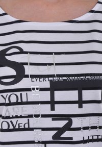 Witte t-shirt met zwarte horizontale strepen en verschillende bedrukte teksten in zilver en zwart, voorzien van een ronde halslijn en korte mouwen.