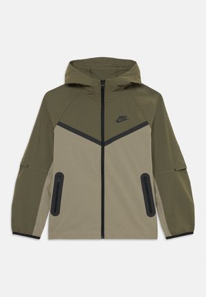 Giacca Nike con cappuccio in oliva e beige, con zip frontale, dettaglio chevron nero, tasche con zip e polsini elastici.