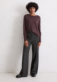 Tumši purpura garās piedurknes adīta blūze, kas apvienota ar pelēkām svītrainām platām biksēm, kurām ir gluda tekstūra un brīvs piegriezums, valkāta ar melniem apaviem.