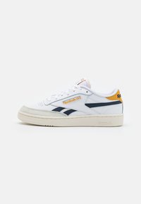 Sneakers bianchi in pelle con accenti blu navy, pannelli laterali testurizzati e suola in gomma beige. Presentano una linguetta con logo giallo sulla linguetta.