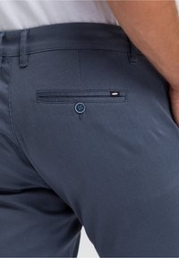 Marinefarbene Netz-Hosen mit einer Gesäßtasche, die mit einem blauen Knopfdetail und subtiler weißer Branding-Akzentuierung an der Taschenverzierung versehen sind. Strukturierter Stoff.