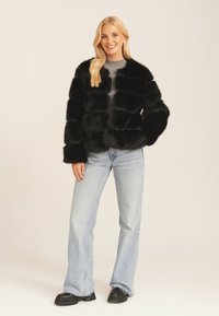 Black faux fur cropped jacket with a boxy design, textured stripes, and a round neckline, paired with light blue jeans and black boots.