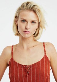 Top in cotone a righe rosse, con dettaglio con lacci sul collo e spalline sottili, realizzato in tessuto leggero con una finitura texture.