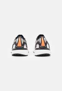 Des chaussures de sport avec un dessus en maille grise, une semelle noire et blanche, et des accents orange au niveau du talon. Présentent un bout arrondi et un dos structuré.