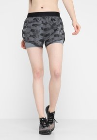 Grå Nike-shorts med resårmidja, med upprepade "NIKE AIR"-logotyper och innerfoder. Bärs med svarta träningsskor.