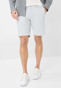 Pantaloni corti in cotone grigio chiaro con una texture liscia, design fino al ginocchio e tasche frontali, abbinati a sneakers bianche.
