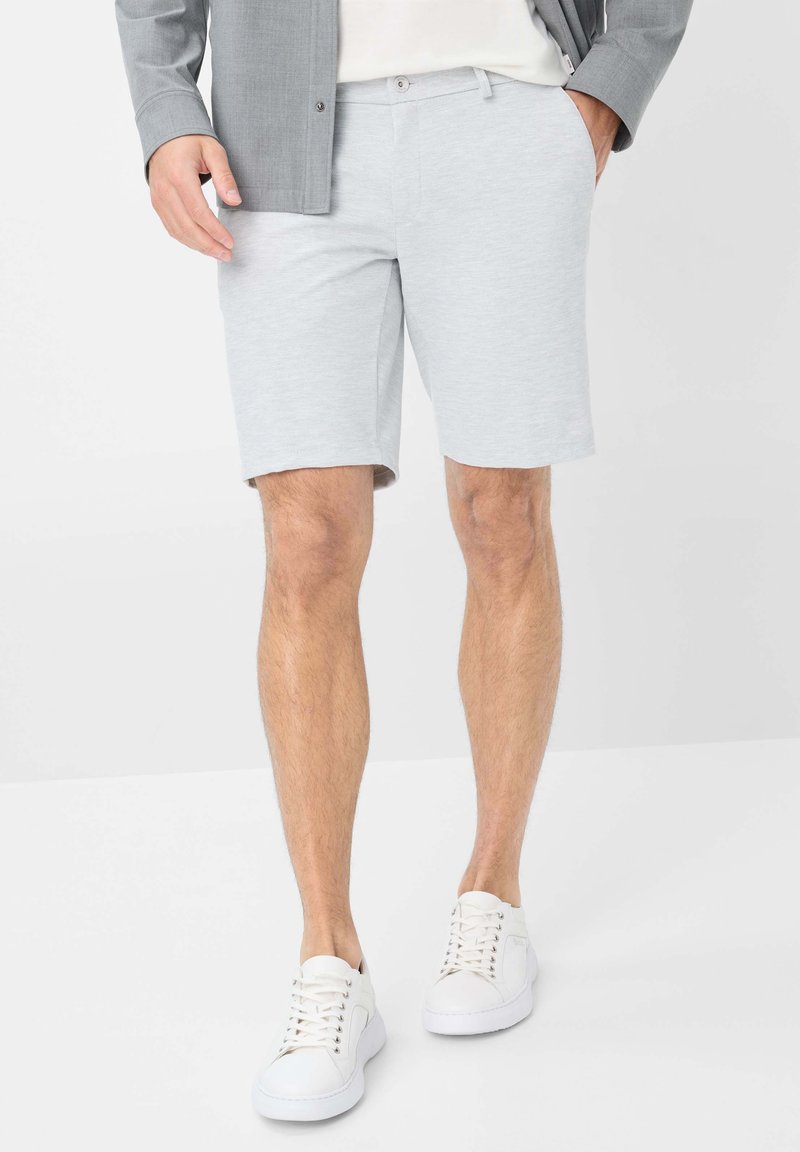 Pantaloni corti in cotone grigio chiaro con una texture liscia, design fino al ginocchio e tasche frontali, abbinati a sneakers bianche.