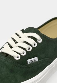 Grüne Wildledersneaker mit weißen Schnürsenkeln, runden Ösen und einer weißen Gummisohle. Verfügt über ein Vans-Logo auf der Seite.