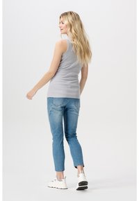 Grijze mouwloze top gecombineerd met lichtblauwe denim jeans. De jeans hebben een aansluitend ontwerp met accentstiksels op de achterzakken.
