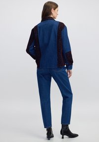 Jeansjack met donkere bloemenaccenten op de schouders en rug, gecombineerd met bijpassende blauwe jeans en zwarte enkellaarsjes met hak.