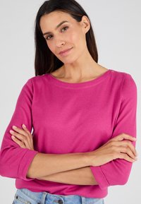 Top rosa de manga larga con cuello redondo, con puños enrollados y botones decorativos en el hombro. Tejido suave y elástico.