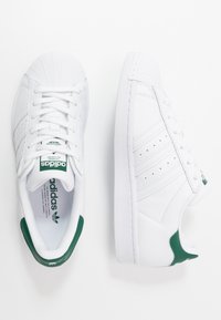 Vita lädersneakers med gröna accenter, som har en texturerad tåskydd, perforerade sidostråk och en klassisk snörningsdesign.