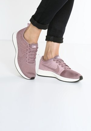 Světle růžové tenisky Nike s prodyšným síťovinovým svrškem, bílou střední podrážkou a černou podrážkou. Zaoblená špička a zavazování na tkaničky s nenápadným označením značky.