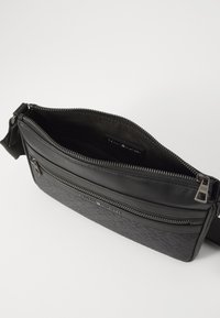 Black crossbody bag with a textured lower section, smooth top, and dual zipper compartments. Made from leather and fabric. Adjustable strap.