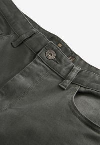 Jean gris foncé en gros plan montrant un bouton, des passants de ceinture et une poche avant avec des coutures visibles et la texture du tissu.