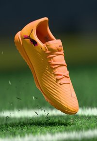 Oranger Sportschuh mit strukturierter Oberseite, erhabenen Rillen und pinken Akzenten. Verfügt über eine Schnürung und eine Gummisohle für guten Halt.