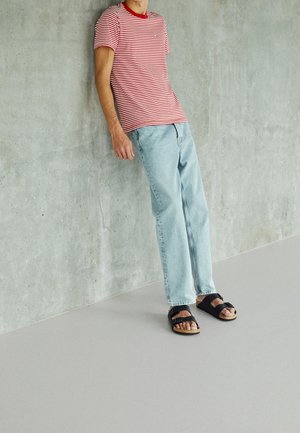 Rød- og hvidstribet t-shirt, lyseblå jeans og sorte sandaler. T-shirten har en rund halsudskæring og korte ærmer, med afslappede jeans.