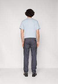 T-shirt à manches courtes bleu clair et pantalon cargo gris foncé avec poches latérales, vu de derrière, associé à des chaussures noires.