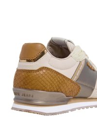 Beige sneaker with brown reptile-textured accents, grey panel, and a metallic heel. Features padded collar and subtle branding on the side.
