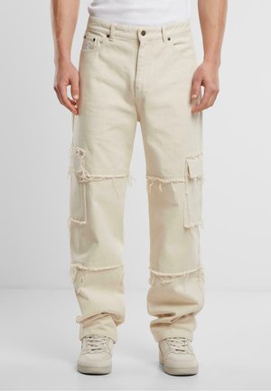 Beige, løse denimbukser med frynser og flere lommepunkter. Har en tradisjonell knapp- og glidelås-stengning.