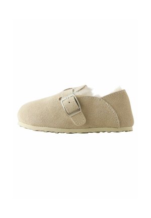 Beige suède pantoffel met een ronde neus, verstelbare zilveren gesp, zachte binnenvoering en een gestructureerde zool voor grip.