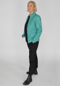 Teal leren jack met een hoge kraag, frontzipper en zijzakken, gecombineerd met zwarte broeken en enkellaarzen. Gladde textuur, nauwsluitend ontwerp.