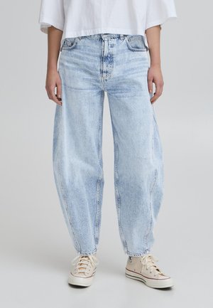 Lyseblå denimjeans med en løs pasform, der har fem-lomme design, synlige sømme og tapered benåbninger. Båret med beige sneakers.