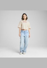 Beige kort T-shirt med rød "Panic Resort" broderi, parret med lyseblå baggy jeans og off-white fuzzy slippers.