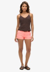 Top in maglia all'uncinetto marrone con spalline sottili e orlo a balze, abbinato a pantaloni di jeans rosa e sandali scuri.