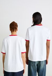 Witte katoenen t-shirts met rode geribbelde kraag en mouwen, vanaf de achterkant gezien, met een relaxte pasvorm en korte mouwen.