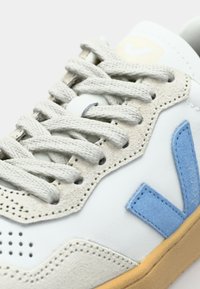 Basket blanche avec des accents bleus et beiges, en daim texturé et cuir lisse, lacets plats, détails perforés et semelle en caoutchouc gomme.