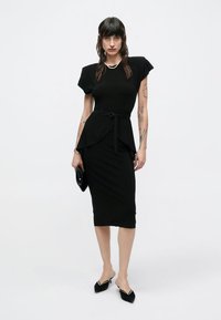 Czarna dopasowana sukienka z krótkimi rękawami, talią z baskinką i paskiem. Gładka faktura, długość do kolan, w zestawie z czarnymi, spiczastymi balerinami i kopertówką.