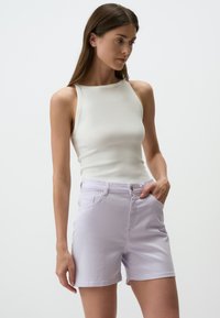 Débardeur blanc à côtes sans manches associé à un short en denim lavande clair avec poches avant et fermeture à bouton.