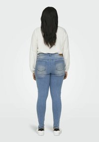 Svetlo modré skinny džínsy so zúženým strihom a vyblednutým umývaním, s vysokým pásom a dvomi zadnými vreckami, skombinované s bielou blúzkou s dlhým rukávom.