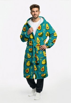 Muž v azúrovo zelenej župane s kapucňou a usmievavými vzormi avokáda, bielymi ponožkami, čiernymi nohavicami a bielym tričkom, pózujúci s rukou na páse.