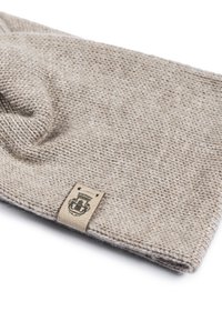 Beige knitted beanie made of soft wool, featuring a textured fabric and a leather tag with embossed logo on one side.
