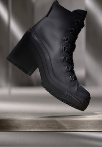 Bottine en cuir noir avec une finition texturée, bout rond et lacets à l'avant. Présente un talon épais en bloquant et une semelle épaisse à motifs.