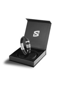 Schwarzes gewebtes Armband mit silbernen Akzenten, präsentiert in einer schwarzen Box mit weicher Innenauskleidung. Verfügt über einen polierten Verschluss und gemusterte Details.
