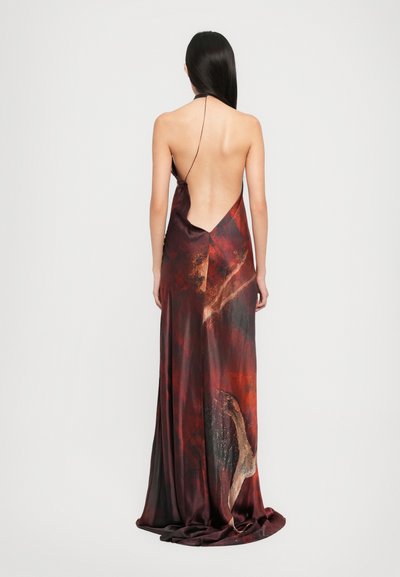 Woman with long dark hair wearing a floor-length backless dress with thin straps, featuring a red and black abstract pattern.