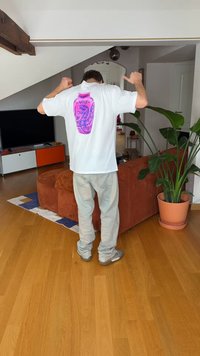 Balti marškinėliai su rožiniu grafiniu dizainu, vaizduojančiu drakoną ir užrašu „NIKE“ ant nugaros, derinami su šviesiai pilkomis kelnėmis ir pilkais batais.