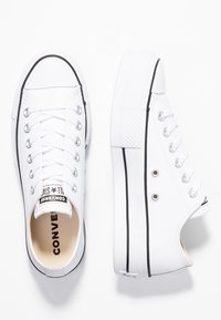 Zapatillas de lona blancas con suelas de goma negras, con diseño de cordones, ojales de metal y una puntera texturizada. Logo visible en el interior.