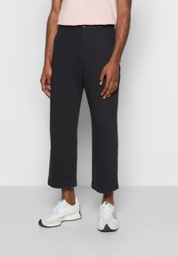 Pantalones cortos negros de algodón, con un corte recto, lazos para cinturón y detalles de costura visibles. Combinados con zapatillas blancas.