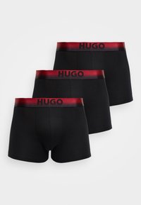 Ensemble de caleçons noirs avec une ceinture élastique rouge arborant le texte "HUGO" en noir. Le tissu semble lisse et extensible.