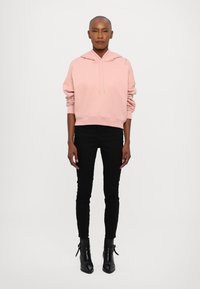 Casaco cropped rosa com cordões, jeans skinny pretos e botas ankle pretas. Tecido suave e corte descontraído com ombros caídos.