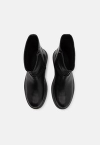 Musta nahkakengät nilkkamallia, joissa on sileä pinta, pyöristetyt varpaat ja sivuvetoketjut. Muotoilu on minimalistinen.