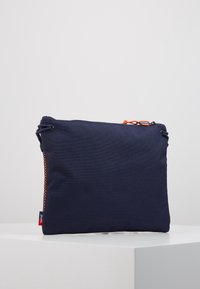 Navy modrý látkový sáček s oranžovou šňůrkou, texturovaný povrch, obdélníkový tvar a kontrastní zipový detail na jedné straně.